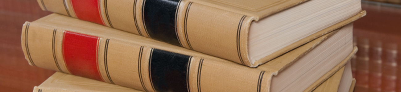 Stack of beige hardcover books with red and black spines on a wooden table, with a bookshelf in the background.